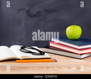 Zurück zum Schulkonzept mit Lesebrille, Bleistifte, Notizblock, Bücher und grünem Apfel mit gelöschten schwarzen Tafel auf desktop Stockfoto