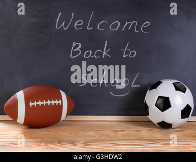 Fußball und Fußball Ball auf Desktop. Gelöschten schwarzen Tafel im Hintergrund zusammen mit Willkommen zurück zu Schule Nachricht an Studenten Stockfoto