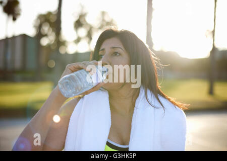 Frau mit Handtuch auf Schultern Trinkwasser aus Kunststoff-Flasche Stockfoto