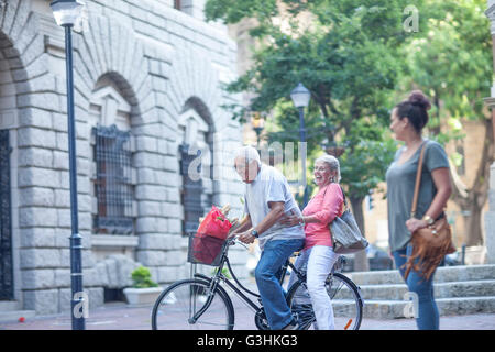 Junge Frau, die gerade älteren Mann und Frau zusammen Radfahren in der Stadt Stockfoto