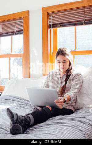 Frau sitzt auf dem Bett mit Laptop Stockfoto