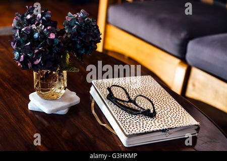 Buchen Sie, lesen Gläser und Blume Anordnung auf Couchtisch Stockfoto