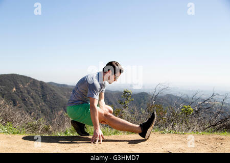 Mann kauert auf Berg tun Bein Dehnübungen Stockfoto