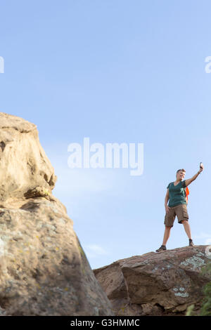 Frau Wanderer stehen oben auf Felsen mit Smartphone zum Selfie nehmen Stockfoto