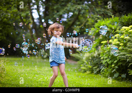 Mädchen winken Blase Zauberstab und die Luftblasen im Garten Stockfoto