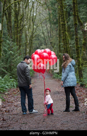 Porträt von weiblichen Kleinkind hält eine Reihe von roten Ballons mit den Eltern im Wald Stockfoto