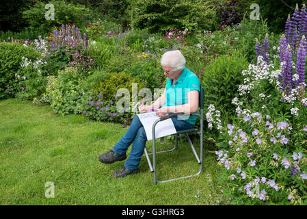 Eine reife Frau entspannt sich in einen Garten mit einem Erwachsenen Malbuch umgeben von Sommerblumen. Stockfoto