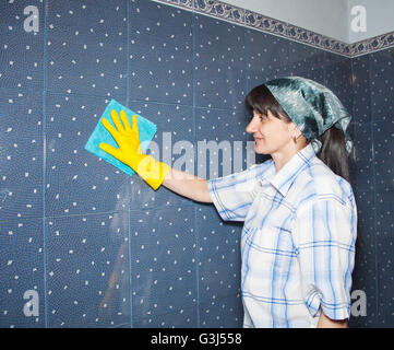lächelnde junge Frau wäscht eine Kachel im Badezimmer Stockfoto