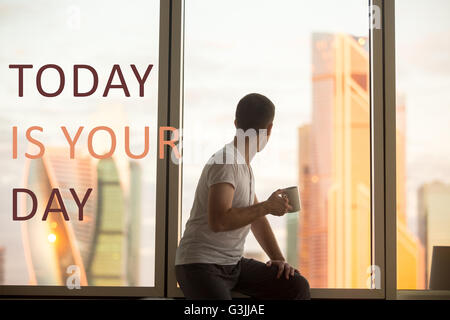 Rückansicht der junge Mann sitzt am Fenster mit Kaffeetasse Dawn Stadt Landschaft betrachten. Schön lässig Kerl entspannend Stockfoto