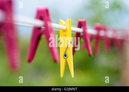 Eine gelbe waschen Peg mit mehreren roten Kunststoff Heringe auf einem weißen Seil-Leine im Freien. Stockfoto