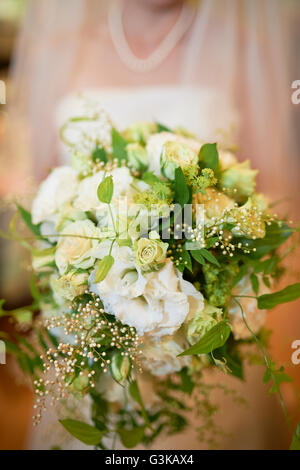 Eine Aufnahme einer Braut vom Hals abwärts unscharf hält einen weißen und grünen Blumenstrauß. Stockfoto