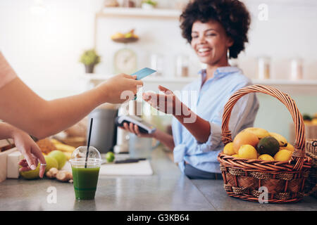 Schuss von einer weiblichen Saft-Bar-Besitzer unter Zahlung von Kunden. Kundin für Saft mit Kreditkarte bezahlen. Stockfoto