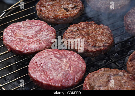 Roh und mittlere selten gekochtes Rind- oder Schweinefleisch Fleisch Grill Burger für Hamburger vorbereitet hautnah auf Rauch Barbeque-Grill, gegrillt Stockfoto