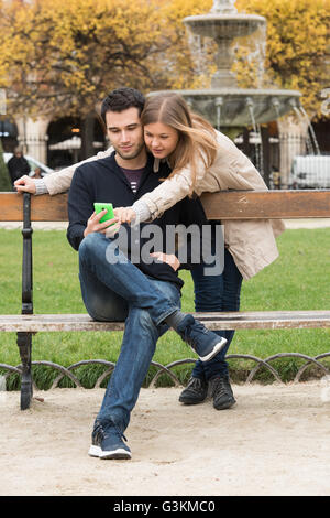 junges Paar im Park, Paris, Frankreich, Blick in Smartphone Stockfoto