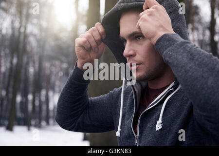 Junger Mann mit Sweatshirt mit Kapuze, im verschneiten, ländlichen Landschaft Stockfoto
