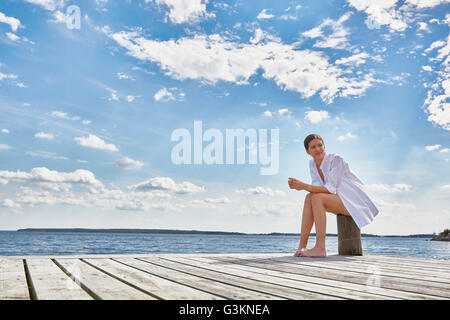 Junge Frau sitzt auf Post auf hölzernen Pier, wegschauen Stockfoto