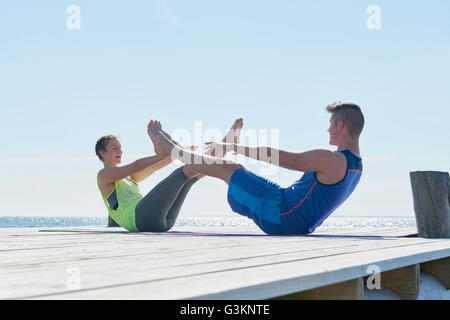 Paar am Pier von Angesicht zu Angesicht, Beine angehoben dabei Sit-Ups Stockfoto