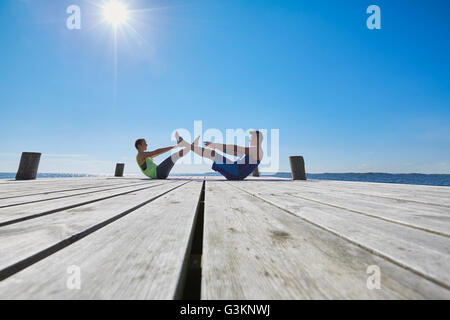 Mitte Abstand Ansicht des Paares auf dem Pier von Angesicht zu Angesicht handeln Sit-Ups Stockfoto