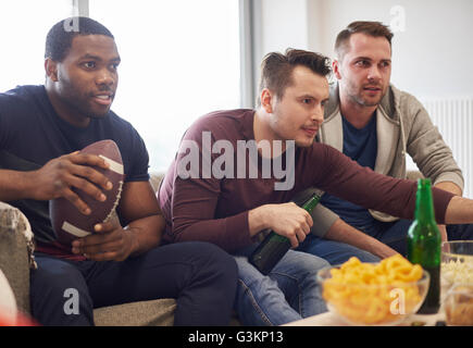 Gruppe von Männern mit Ball beobachten Sportereignis im Fernsehen mit Snacks und Bier Stockfoto