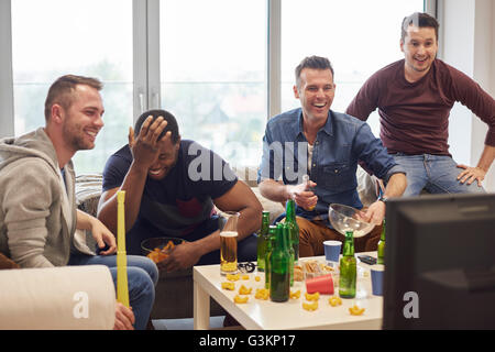 Gruppe von Männern beobachten Sportereignis im Fernsehen mit Snacks und Bier lächelnd Stockfoto