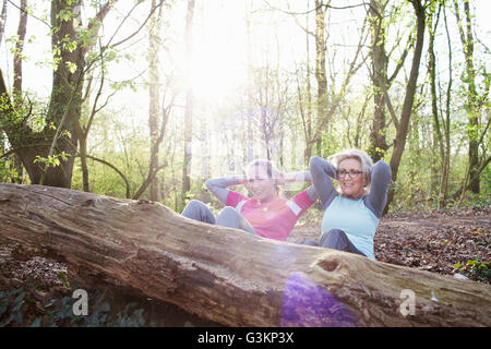 Frauen im Wald Hände hinter Kopf tun Sit up gegen umgestürzten Baum Stockfoto