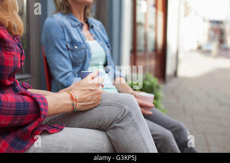 Frauen sitzen auf Stühlen vor Geschäft halten Kaffeetassen davon abgeschnitten Stockfoto