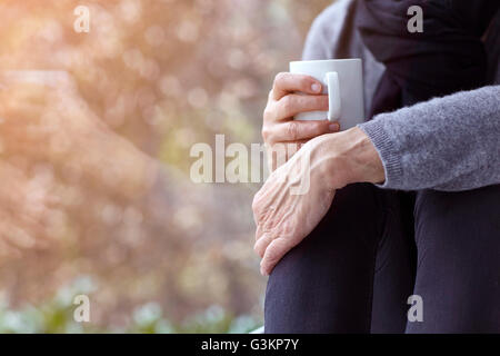 Blick auf Frau Fenster halten Kaffeetasse umarmt Knien sitzen abgeschnitten Stockfoto