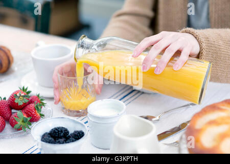 Blick auf Frau Gießen Orangensaft aus der Flasche ins Glas beschnitten Stockfoto
