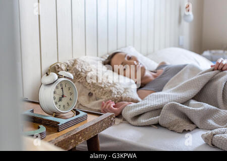 Frau im Bett, Wecker auf dem Nachttisch Stockfoto