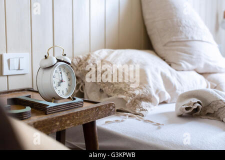 Ungemachten Bett, Wecker auf dem Nachttisch Stockfoto