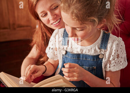 Nahaufnahme von Mitte Erwachsene Frau Buch mit Tochter auf Sessel Stockfoto