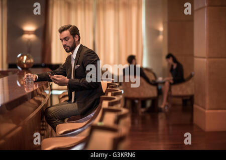 Junger Geschäftsmann sitzt an der Hotelbar Smartphone Texte lesen Stockfoto