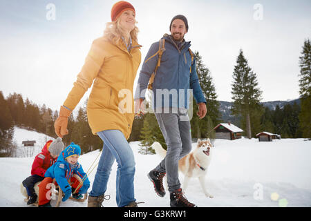 Eltern ziehen Söhne am Schlitten in Winterlandschaft, Elmau, Bayern, Deutschland Stockfoto