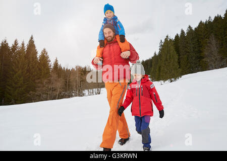 Junger Mann Schulter zu tragen und zu Fuß mit Söhnen in Schnee bedeckt Landschaft, Elmau, Bayern, Deutschland Stockfoto