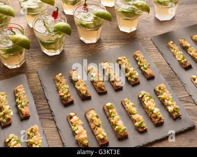 Guacamole, Räucherlachs und Roggen Brot Kanapees mit Wodka-cocktail mit Limettenscheiben garniert Stockfoto