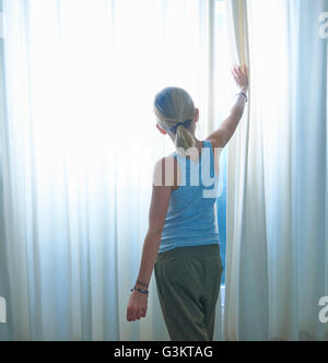 Rückansicht des Mädchens spähte durch net verhangenen Fenster Stockfoto