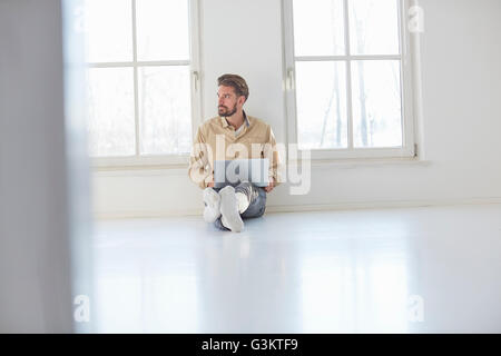 Junger Mann am Boden mit Laptop in leeren neuen Zuhause Stockfoto