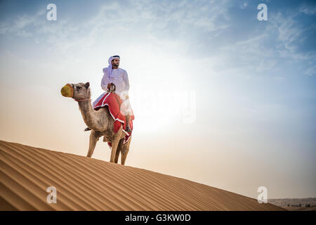 Mann trägt traditionelle Naher Osten Kleidung Reiten Kamel in der Wüste, Dubai, Vereinigte Arabische Emirate Stockfoto