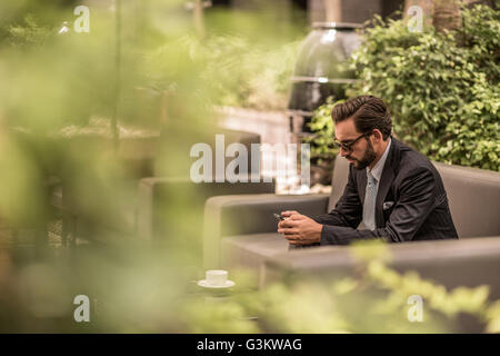 Geschäftsmann lesen Smartphone Texte auf Gartensofa Hotel, Dubai, Vereinigte Arabische Emirate Stockfoto