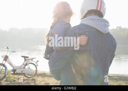 Vater Holding Tochter, neben See, Vater tragen Helm, Rückansicht Stockfoto