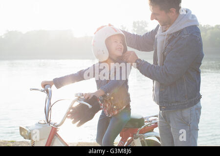 Junge Mädchen sitzen auf Vaters Moped, Vater Tochter Kopf, Helm aufsetzen, Lächeln Stockfoto