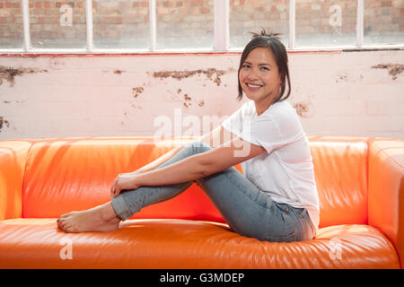 Frau sitzt auf dem Sofa mit ihren Füßen entspannt und lächelnd