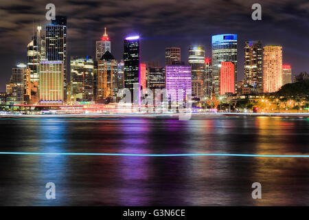 Helle Wand der Wolkenkratzer in der Stadt Sydney CBD über Circular Quay durch den Hafen von unscharfen Gewässern nachts reflektieren Licht in wa Stockfoto