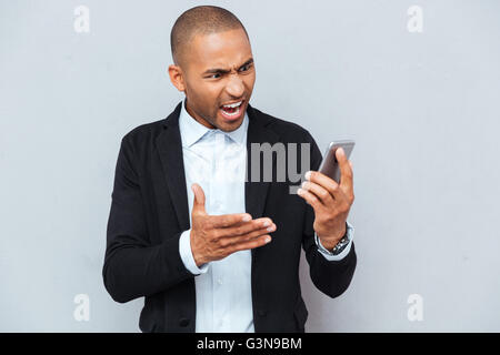 Close-up Portrait von zorniger junger Mann zeigt mit Finger auf seinem Smartphone isoliert grau hinterlegt Stockfoto