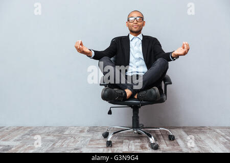 Entspannte schöne afrikanische junger Mann sitzen und meditieren auf Bürostuhl Stockfoto