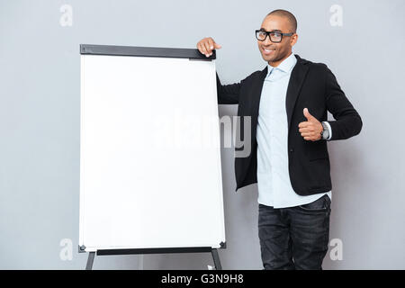Lächelnd afroamerikanischen jungen Geschäftsmann stehen in der Nähe von Flipchart und Daumen nach oben zeigen Stockfoto