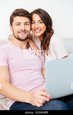 Glückliches junges Paar sitzt auf der Couch mit Laptop isoliert auf weißem Hintergrund Stockfoto