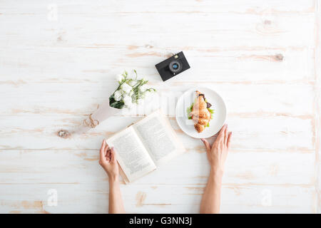 Weibliche Hände halten Buch und Platte auf dem Schreibtisch aus Holz Stockfoto