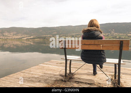 Schöne Mädchen auf einer Bank am See suchen Stockfoto