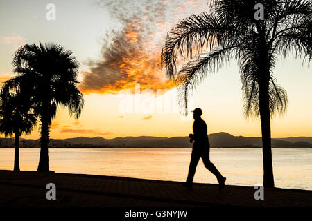 Silhouette eines Mannes läuft auf dem Bürgersteig der Beira Mar Norte Avenue bei Sonnenuntergang. Florianopolis, Santa Catarina, Brasilien. Stockfoto